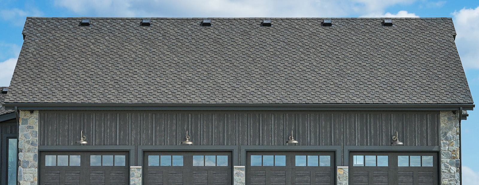 Wide garage with grey architectural shingle roof, dark board-and-batten siding and stone accents.