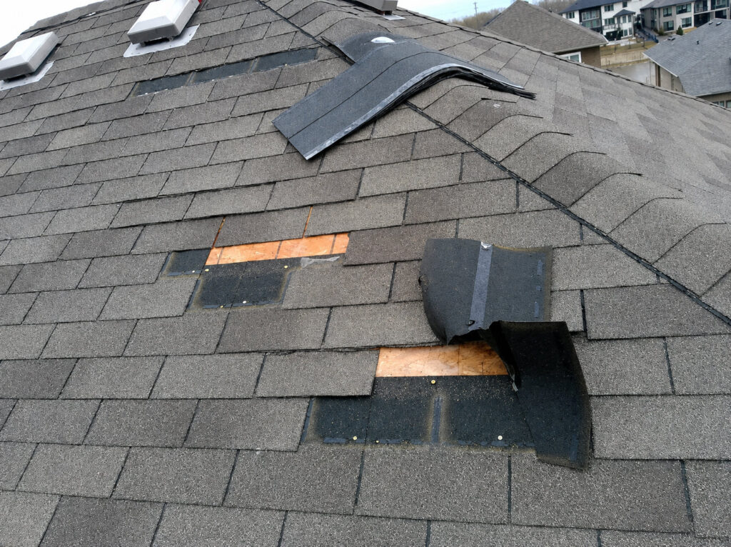 Damaged asphalt shingle roof with missing and lifted shingles exposing the roof deck.