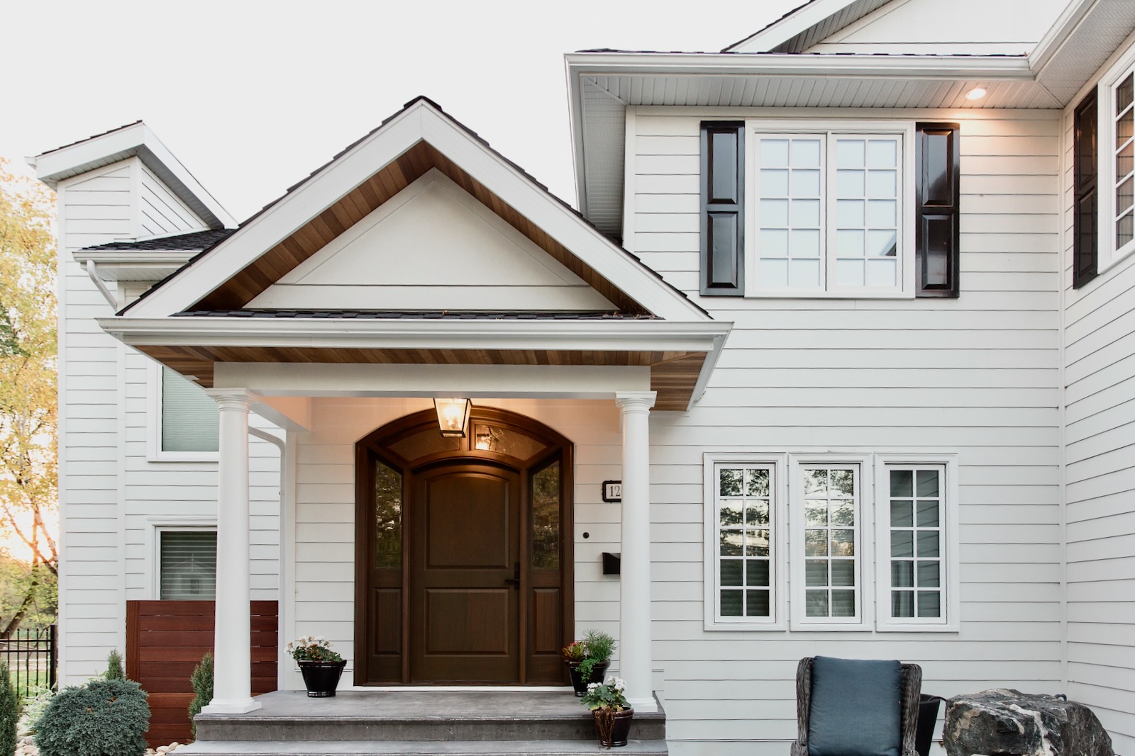 White lap siding home with gabled entry portico, wood soffit and dark-shuttered windows.
