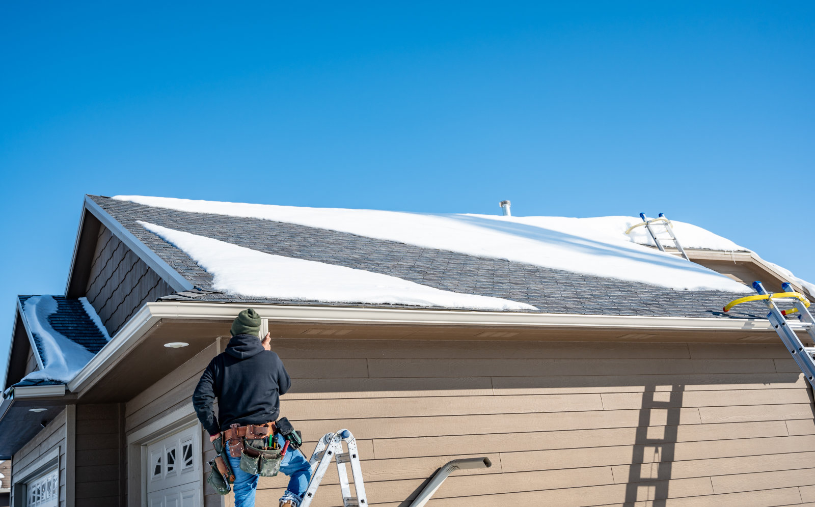Roofer inspects snow-covered home roof with ladders in place