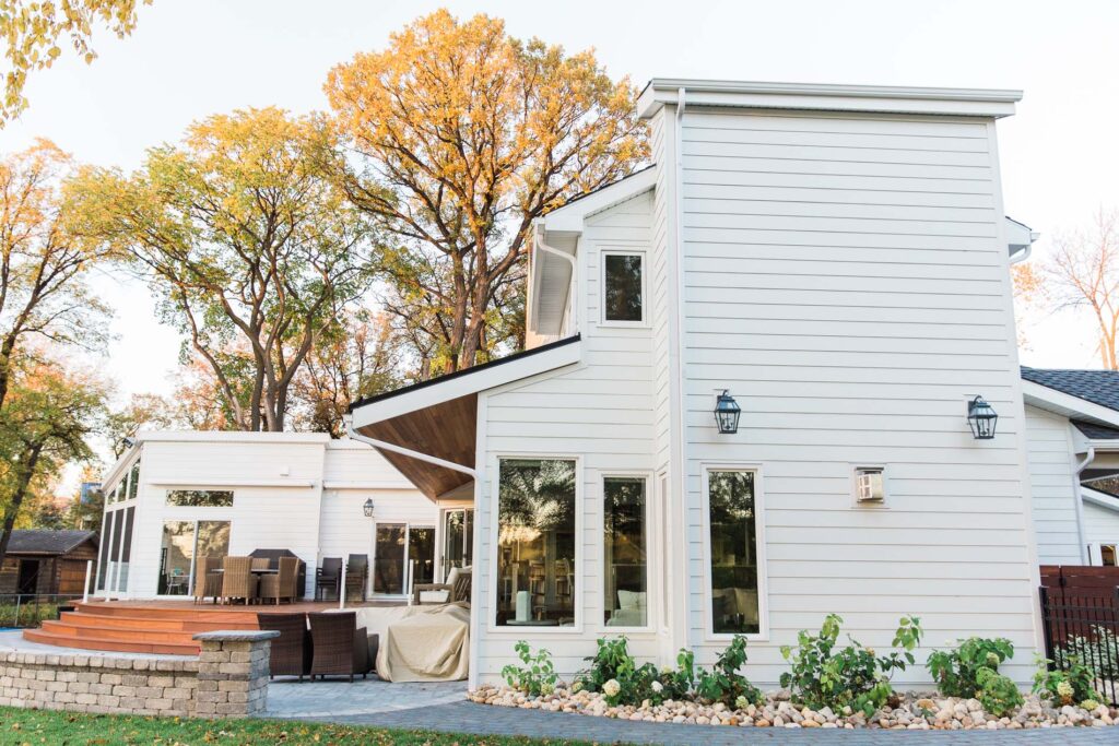 Modern white home exterior with horizontal siding, large windows, and a backyard patio deck