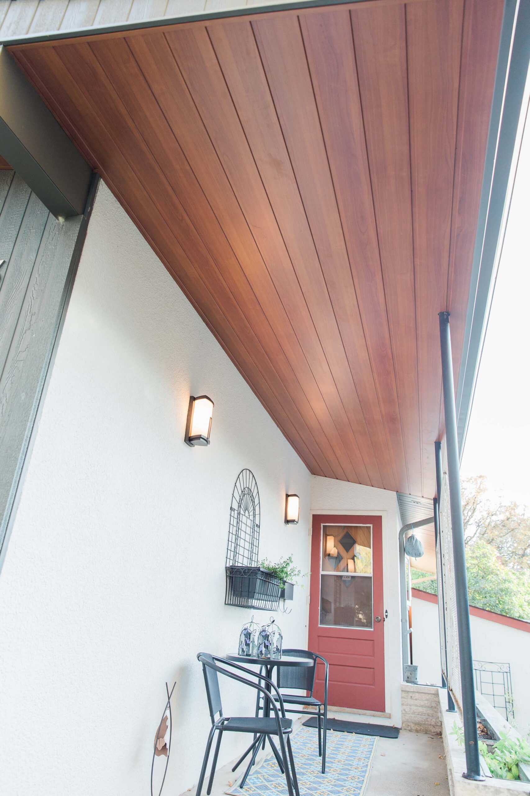Warm wood-panelled soffit over an entry porch with downspout and red door.