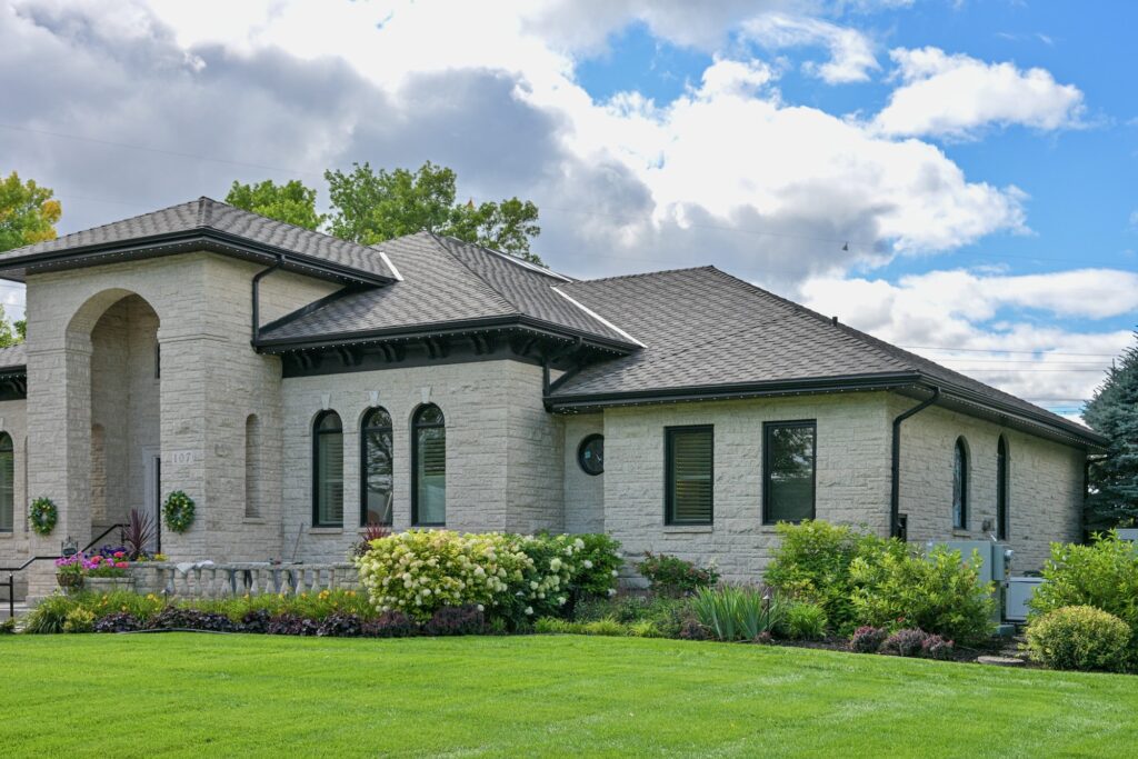 Large stone home with a dark shingle roof and landscaped front yard