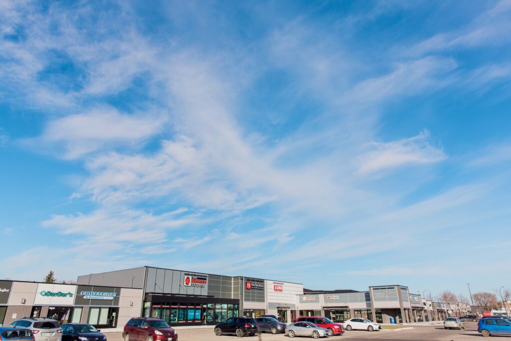 A full view of the large strip mall with a number of retail store fronts and parking lot.
