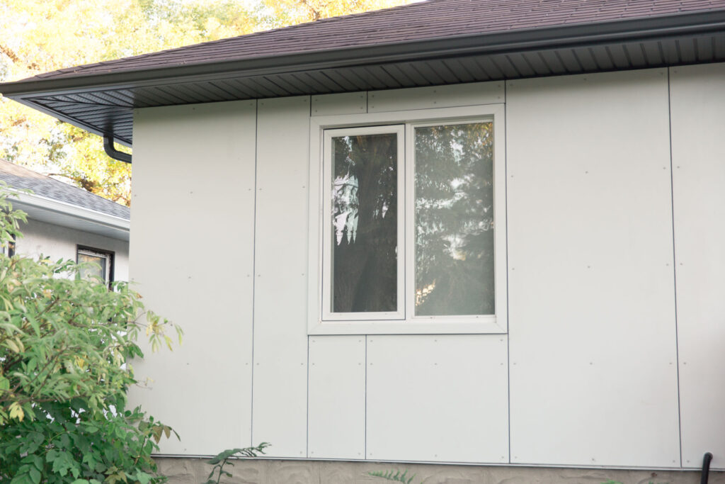 White panel siding beneath dark soffits beside a front window