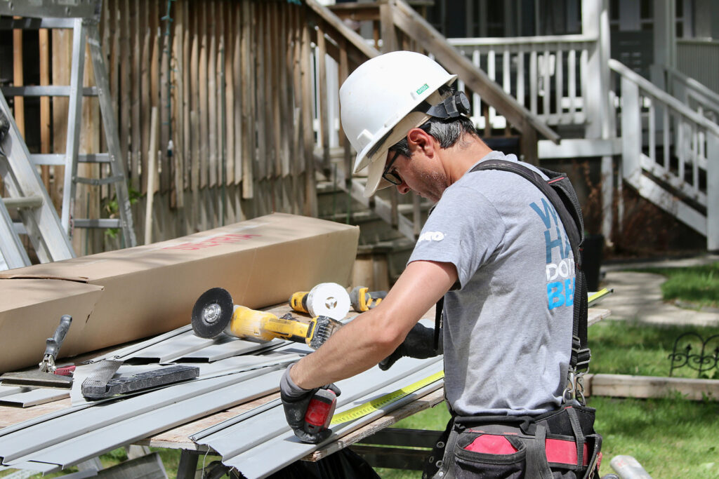Siding installer measures and prepares metal panels at a worksite