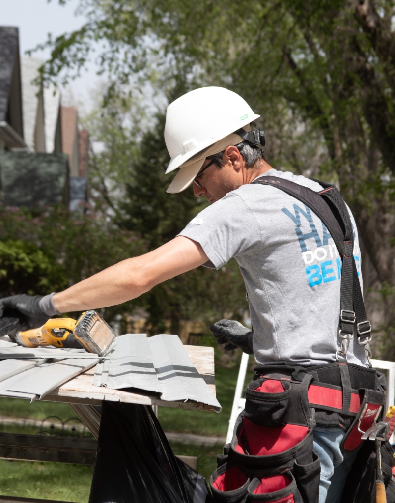Roofer wearing safety gear cuts metal roofing panels at a job site