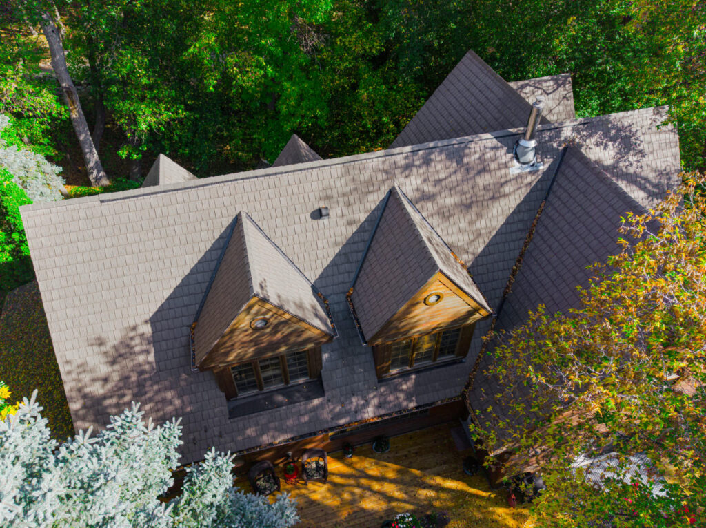 Aerial view of a shingled home roof with dormers among mature trees