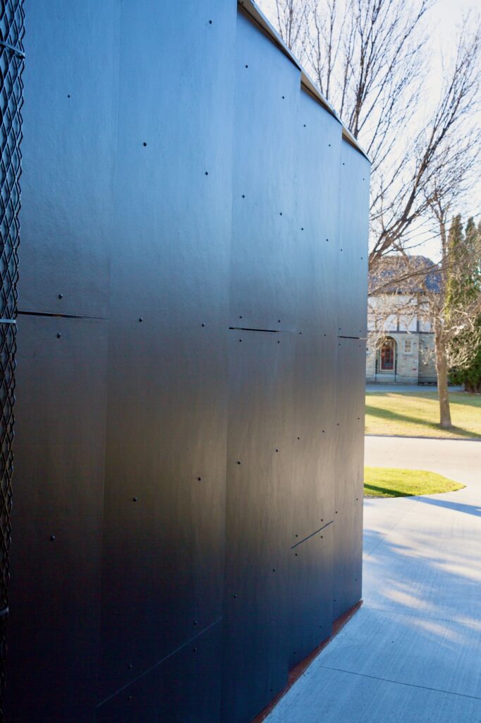Dark metal exterior wall beside a concrete driveway and front yard